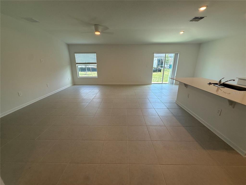 An open-concept living area features light-colored tile flooring, a kitchen island, and sliding glass doors — 3228 ALPINE WAY, DAVENPORT, FL
