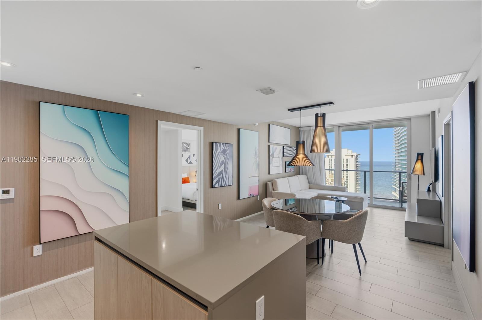 A modern living and dining area features a kitchen island, ocean views, and neutral decor — 4010 S Ocean Dr # R2005, Hollywood FL 33019, HOLLYWOOD, FL