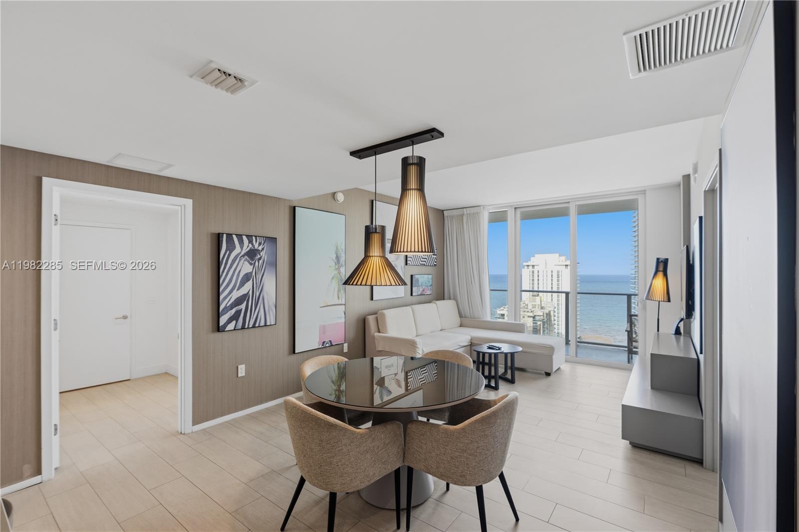 A modern living and dining area features a glass table, neutral furniture, and ocean views — 4010 S Ocean Dr # R2005, Hollywood FL 33019, HOLLYWOOD, FL