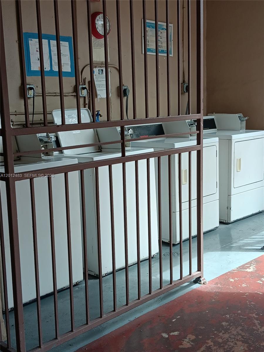 A laundry room features several white washing machines behind a brown metal security gate — 652 NW 3rd St # 103, Miami FL 33128, MIAMI, FL