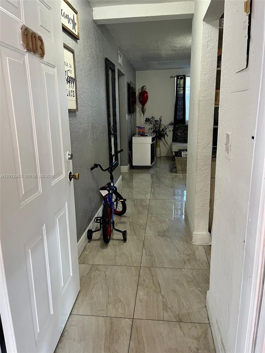 A tiled hallway leads from an entryway door past a bicycle toward a living area — 652 NW 3rd St # 103, Miami FL 33128, MIAMI, FL