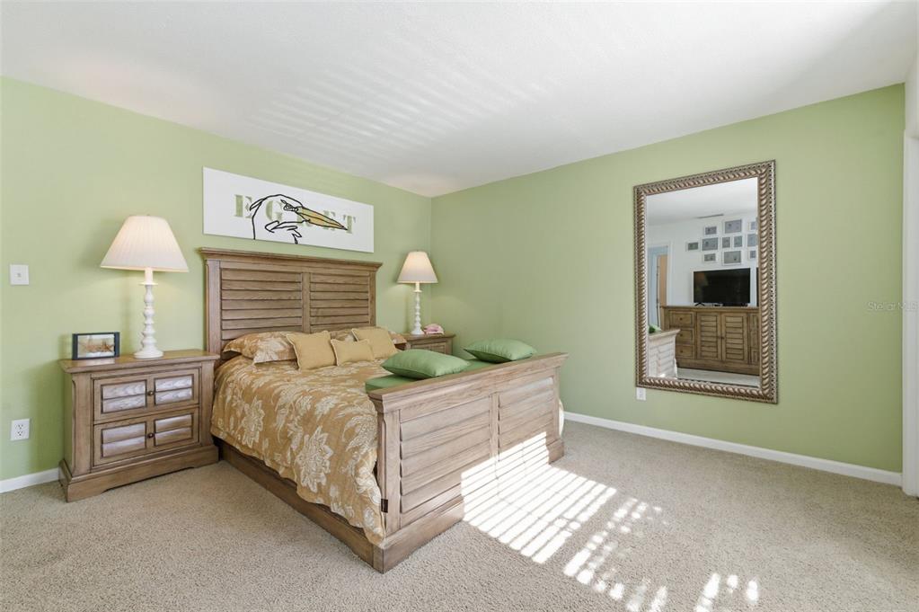 A bedroom features light green walls, a wooden bed frame, and a large wall mirror — 5005 COQUINA KEY DRIVE SE UNIT E, ST PETERSBURG, FL