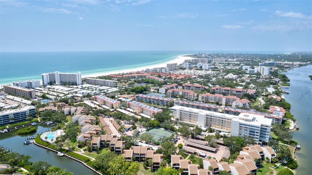 An aerial view shows a coastal resort complex with multiple buildings, swimming pools, and waterways — 1700 COVE II PLACE UNIT 310, SARASOTA, FL