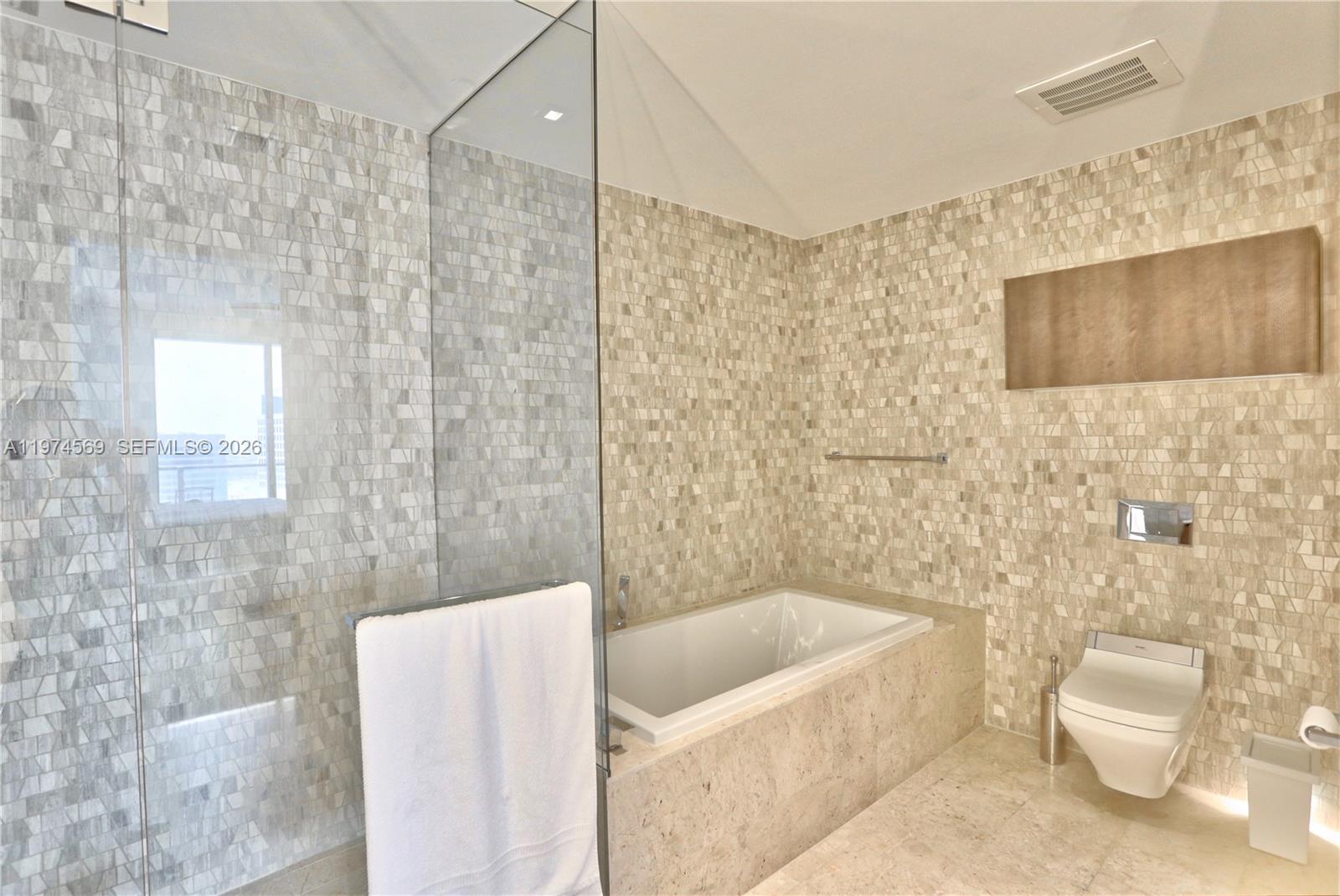 A modern bathroom features a glass-enclosed shower, a built-in bathtub, and beige mosaic tile walls — 88 SW 7th St # 3805, Miami FL 33130, MIAMI, FL