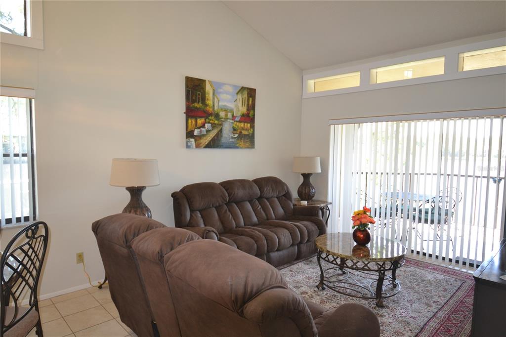A living room features a brown reclining sofa, a round coffee table, and vertical blinds — 336 WOODLAKE WYNDE, OLDSMAR, FL