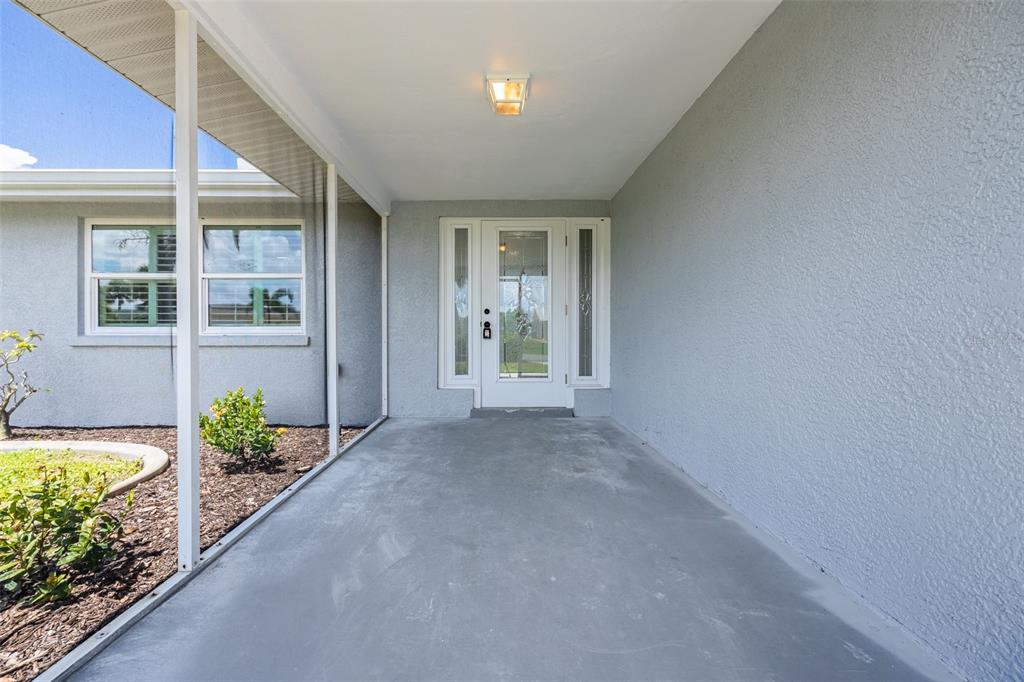 A covered concrete porch leads to a white front door with glass sidelights — 1464 DEER CREEK DRIVE, ENGLEWOOD, FL