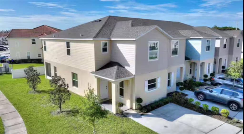 An exterior view of a two-story beige townhouse with a driveway and small front lawn — 4877 CORAL CASTLE DRIVE, KISSIMMEE, FL