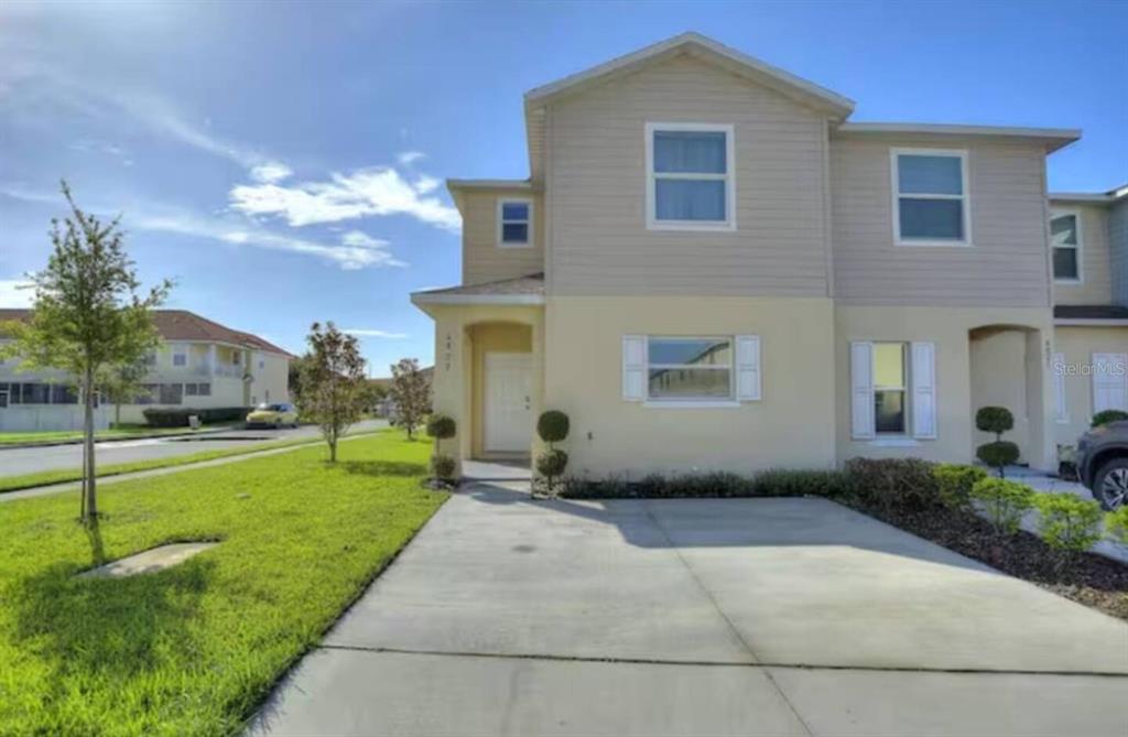 A two-story tan townhouse with a concrete driveway and a small front lawn — 4877 CORAL CASTLE DRIVE, KISSIMMEE, FL