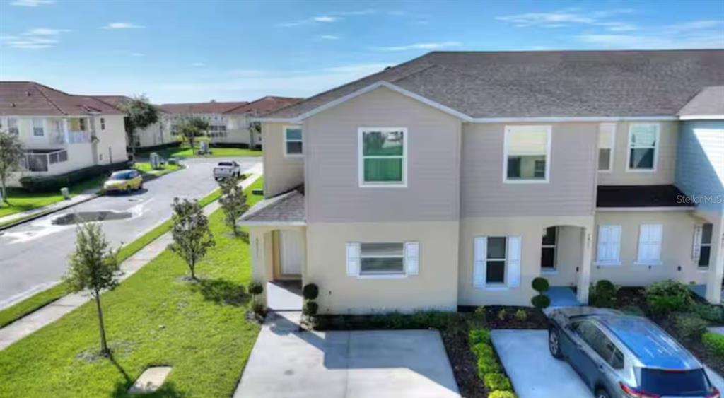 An exterior view of a two-story townhouse with a concrete driveway and a grassy lawn — 4877 CORAL CASTLE DRIVE, KISSIMMEE, FL