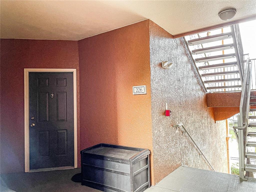 An exterior view of a residential apartment entrance with a dark door and metal stairs — 6149 METROWEST BOULEVARD UNIT 206, ORLANDO, FL
