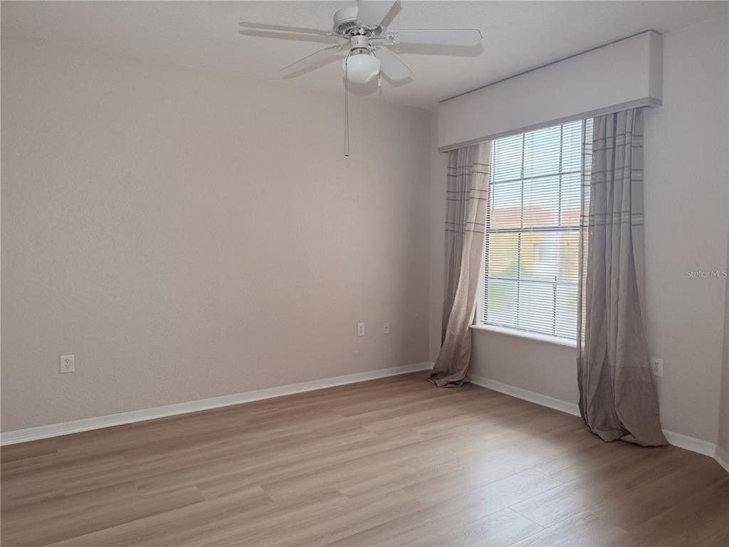 An empty room features light wood-look flooring, a ceiling fan, and a window with curtains — 6149 METROWEST BOULEVARD UNIT 206, ORLANDO, FL