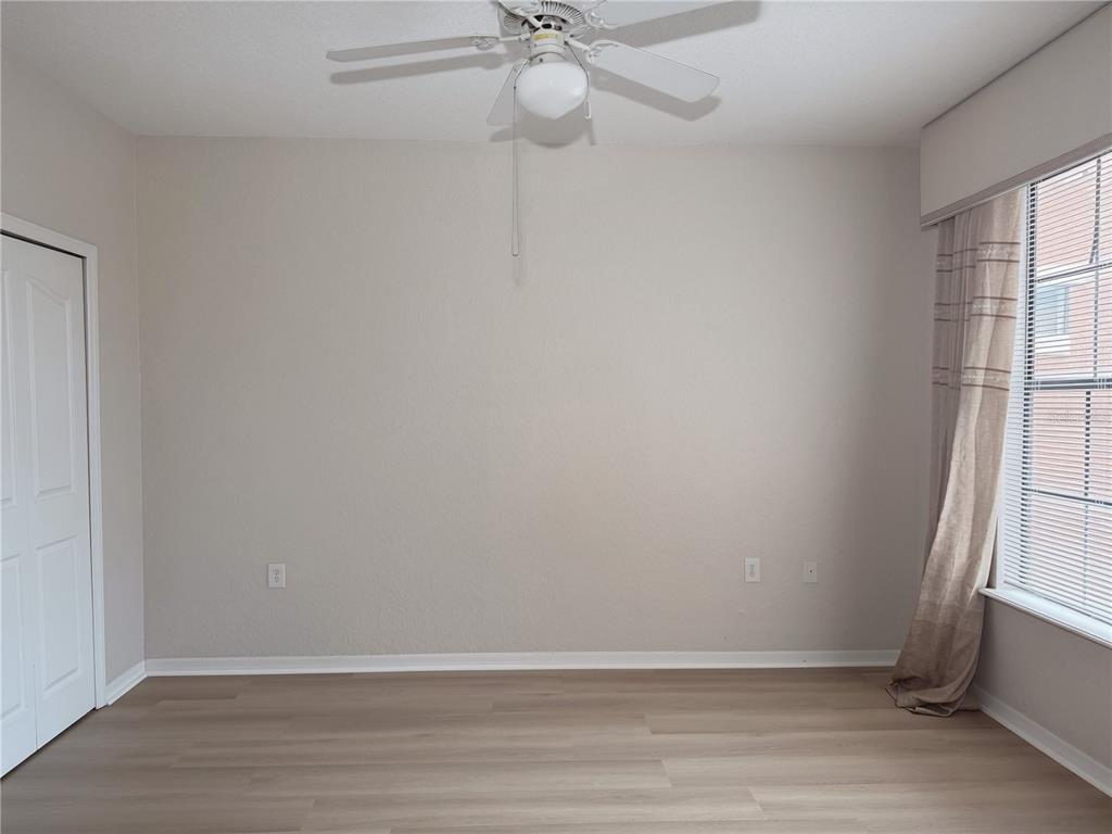 An empty room features light-colored walls, wood-look flooring, a ceiling fan, and a window — 6149 METROWEST BOULEVARD UNIT 206, ORLANDO, FL