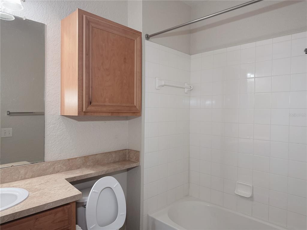 A bathroom features a vanity with a mirror, a wooden cabinet, and a tiled shower-tub — 6149 METROWEST BOULEVARD UNIT 206, ORLANDO, FL