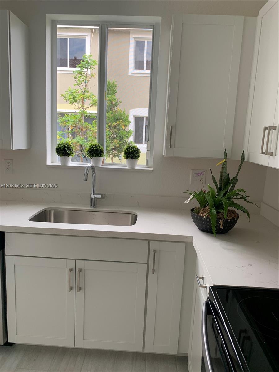 A kitchen sink area features white cabinets, a quartz countertop, and a window view — 1068 SE 24th Ave, Homestead FL 33035, HOMESTEAD, FL