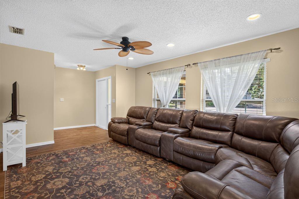 A living room features a large brown leather sectional, a patterned rug, and windows with curtains — 3110 CLOVEWOOD PLACE, SEFFNER, FL