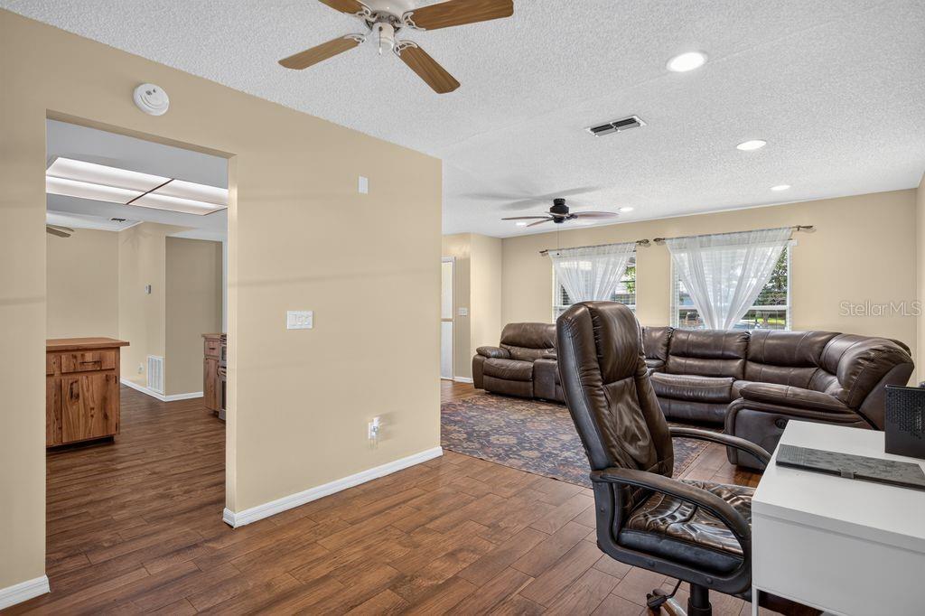 A living room with wood-look flooring, a leather sectional, and an adjacent kitchen area — 3110 CLOVEWOOD PLACE, SEFFNER, FL