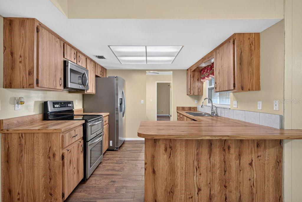 A kitchen features wood-grain cabinets, laminate countertops, stainless steel appliances, and wood-look flooring — 3110 CLOVEWOOD PLACE, SEFFNER, FL