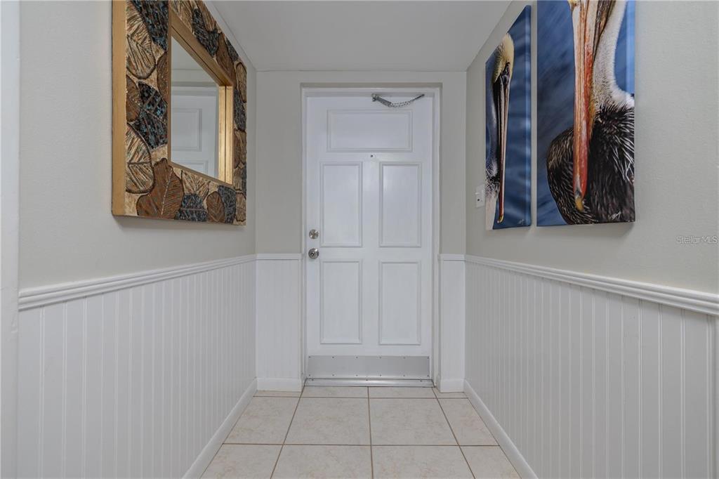 A tiled entryway features white wainscoting, a decorative mirror, and two pelican wall art pieces — 4501 S ATLANTIC AVENUE UNIT 415, NEW SMYRNA BEACH, FL