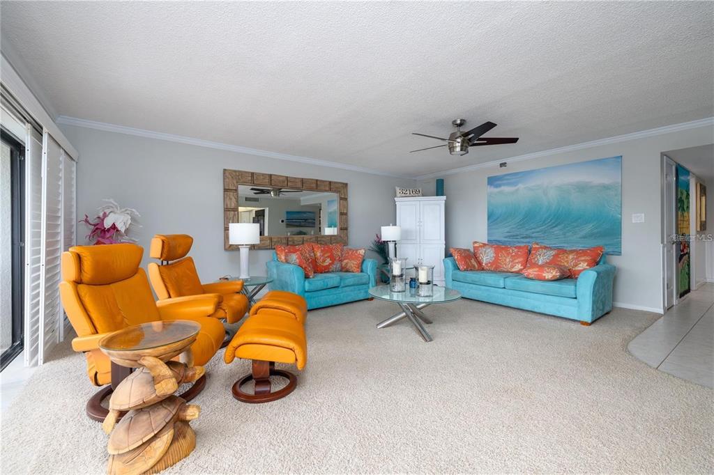 A living room features bright blue sofas, orange leather recliners, and a large wave mural — 4501 S ATLANTIC AVENUE UNIT 415, NEW SMYRNA BEACH, FL