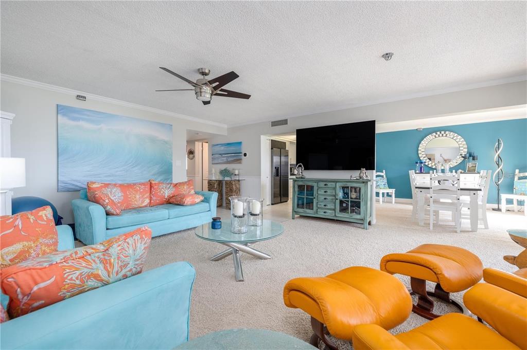 A living room with blue sofas, orange accent pillows, a television, and a dining area — 4501 S ATLANTIC AVENUE UNIT 415, NEW SMYRNA BEACH, FL