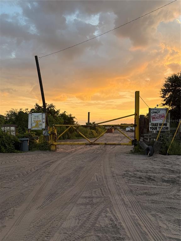A yellow metal gate blocks a sandy dirt road at sunset — HOLOPAW GROVES ROAD Lot 125 & 126, ST CLOUD, FL