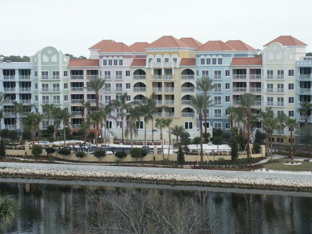 A multi-story, pastel-colored apartment building stands behind a swimming pool and a waterfront area — 102 YACHT HARBOR DRIVE UNIT 161, PALM COAST, FL