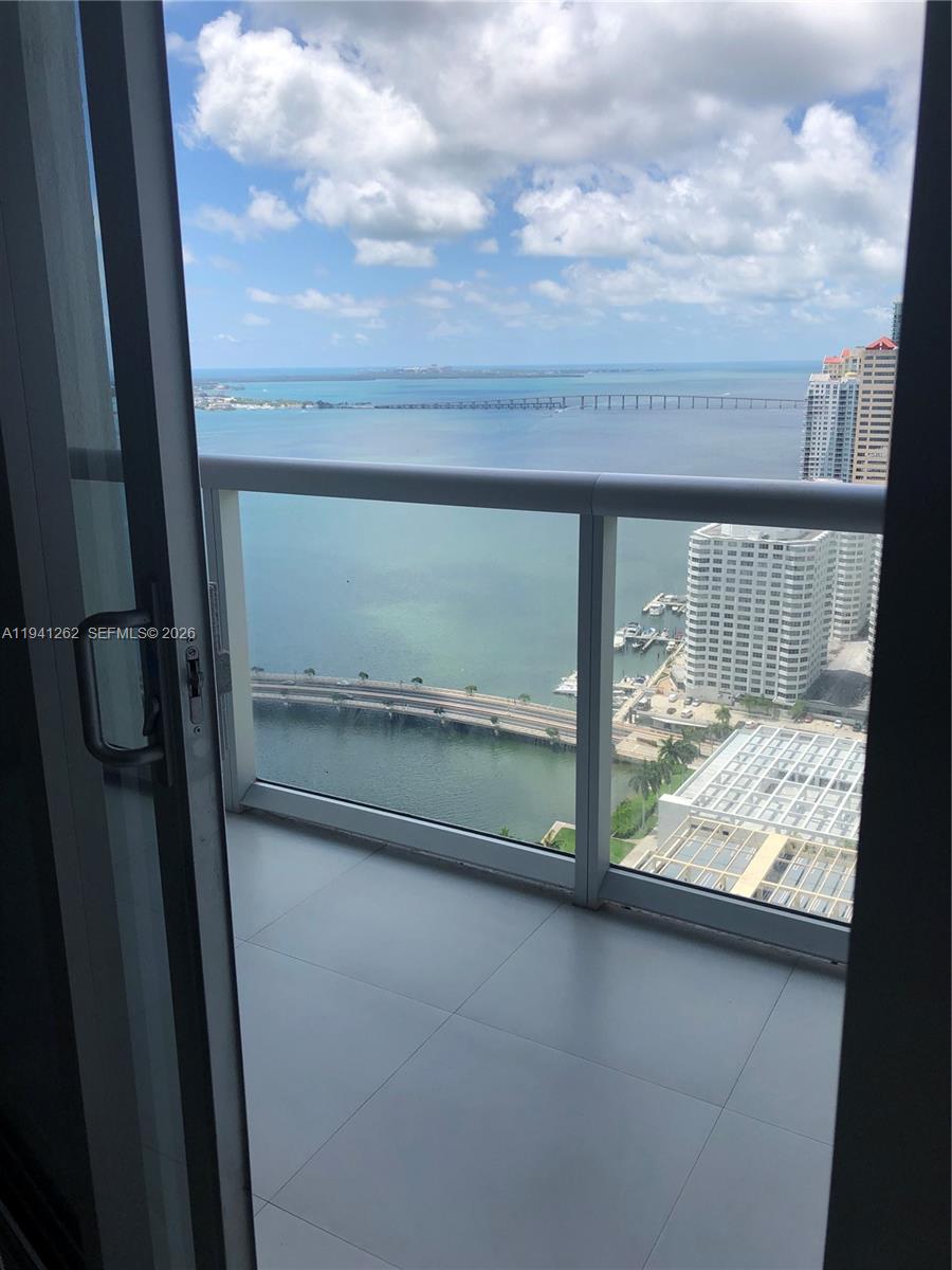A balcony with a glass railing overlooks a bay, a bridge, and city buildings — 495 Brickell Ave # 3507, Miami FL 33131, MIAMI, FL