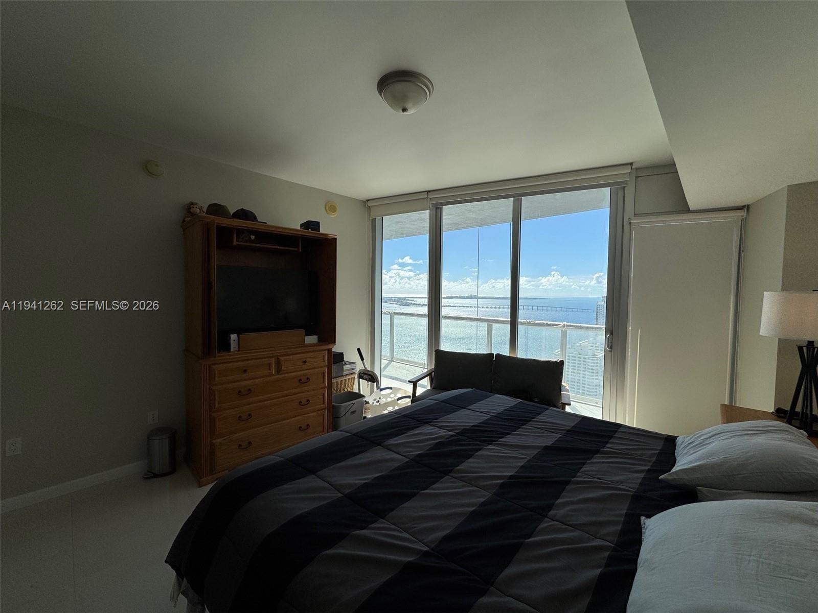 A bedroom features a striped bed, a wooden armoire, and floor-to-ceiling windows overlooking the ocean — 495 Brickell Ave # 3507, Miami FL 33131, MIAMI, FL