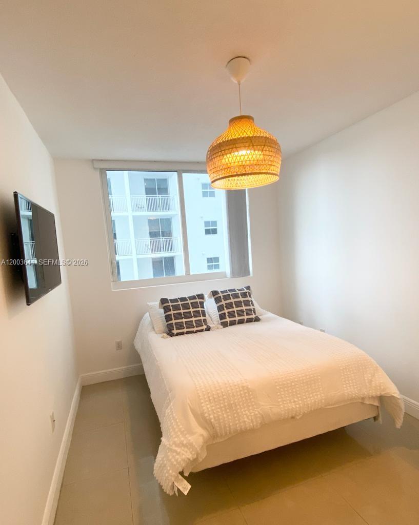 A bedroom features a bed with white bedding, two patterned pillows, and a woven pendant light — 170 SE 14th St # 1504, Miami FL 33131, MIAMI, FL