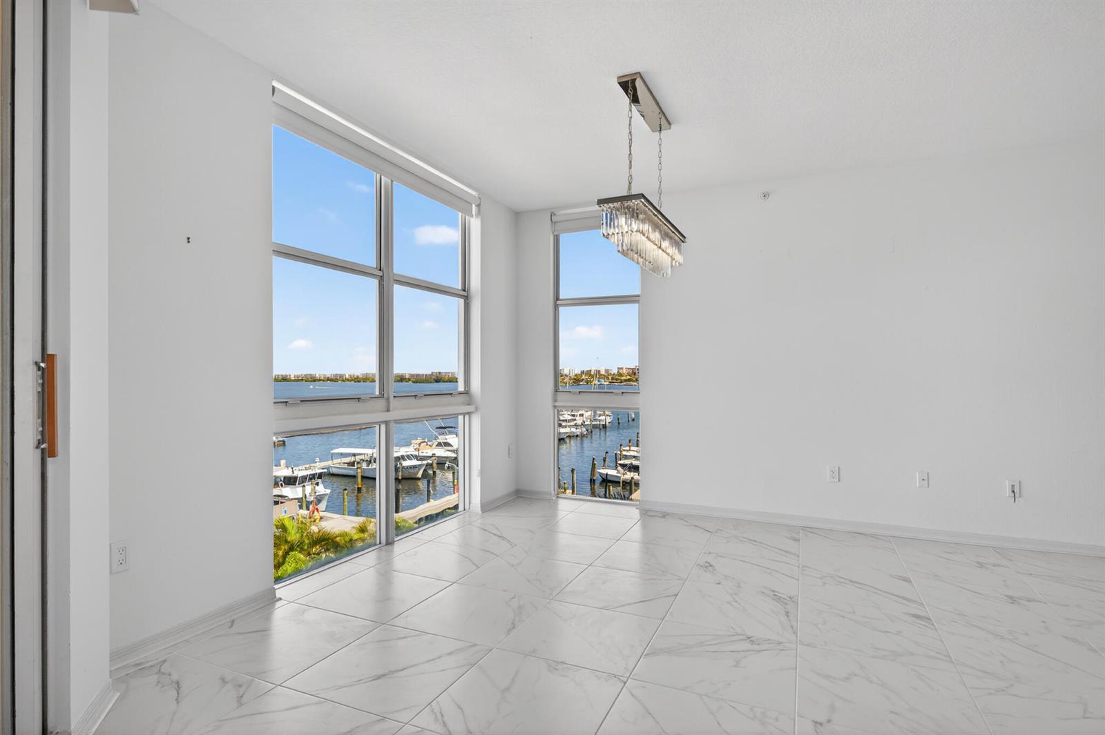 An empty room with white marble floors, a crystal chandelier, and large windows overlooking a marina — 806 E Windward Way # 403, Lantana FL 33462, LANTANA, FL