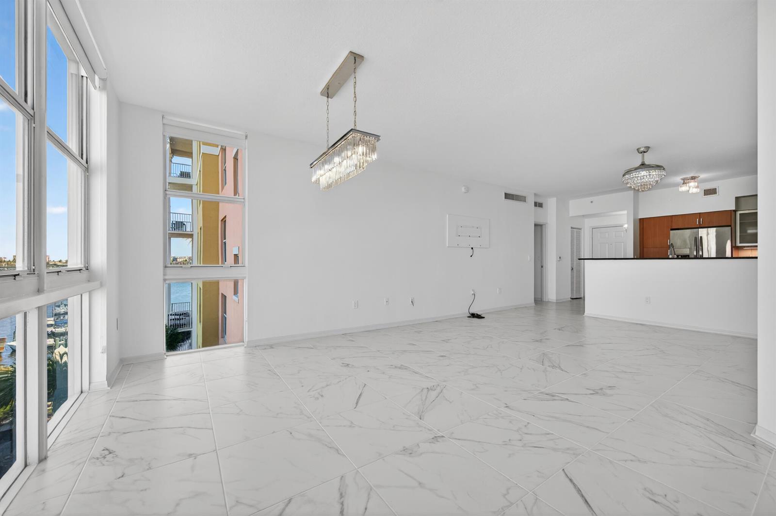 An open-concept living area features white marble-look tile floors, a crystal chandelier, and large windows — 806 E Windward Way # 403, Lantana FL 33462, LANTANA, FL