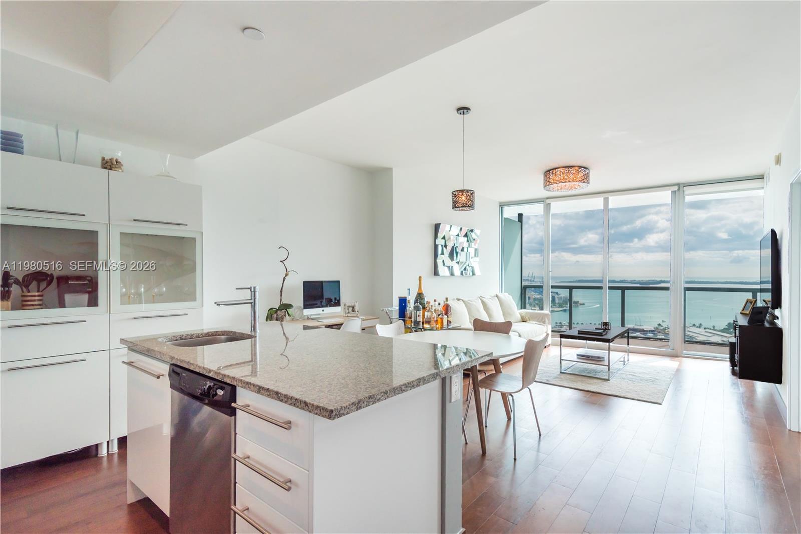 A modern kitchen and living area feature white cabinetry, granite countertops, and floor-to-ceiling windows — 888 Biscayne Blvd # 3506, Miami FL 33132, MIAMI, FL