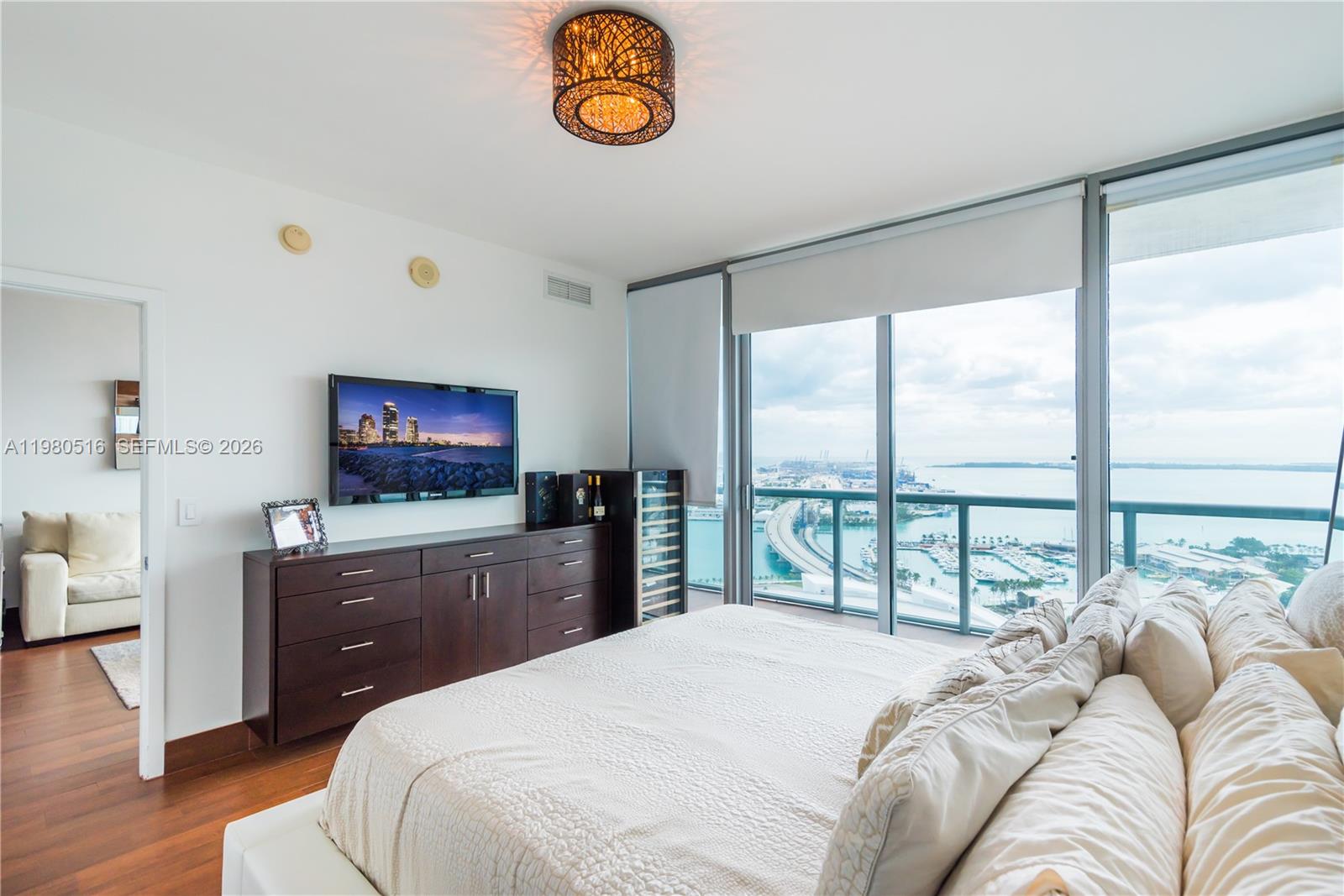A bedroom features a bed, dark wood dresser, television, and floor-to-ceiling windows overlooking a harbor — 888 Biscayne Blvd # 3506, Miami FL 33132, MIAMI, FL