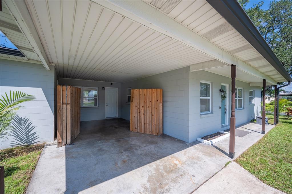A gray concrete block house features a covered carport with wooden privacy screens and porch — 2903 STANHOPE AVENUE, LAKELAND, FL