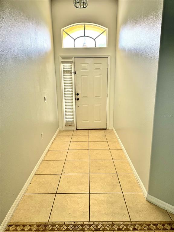 An entryway features a white front door, a transom window, and light-colored tile flooring — 1944 THE OAKS BOULEVARD, KISSIMMEE, FL