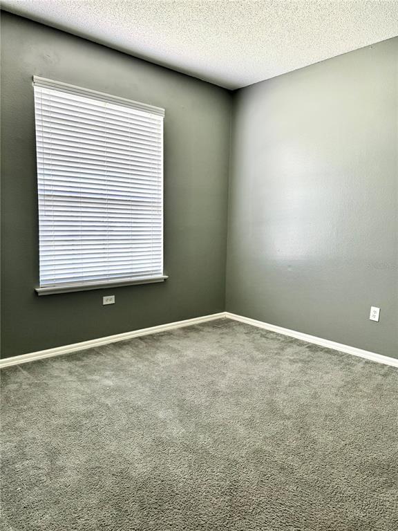 An empty room features dark gray walls, gray carpeting, and a window with white blinds — 1944 THE OAKS BOULEVARD, KISSIMMEE, FL