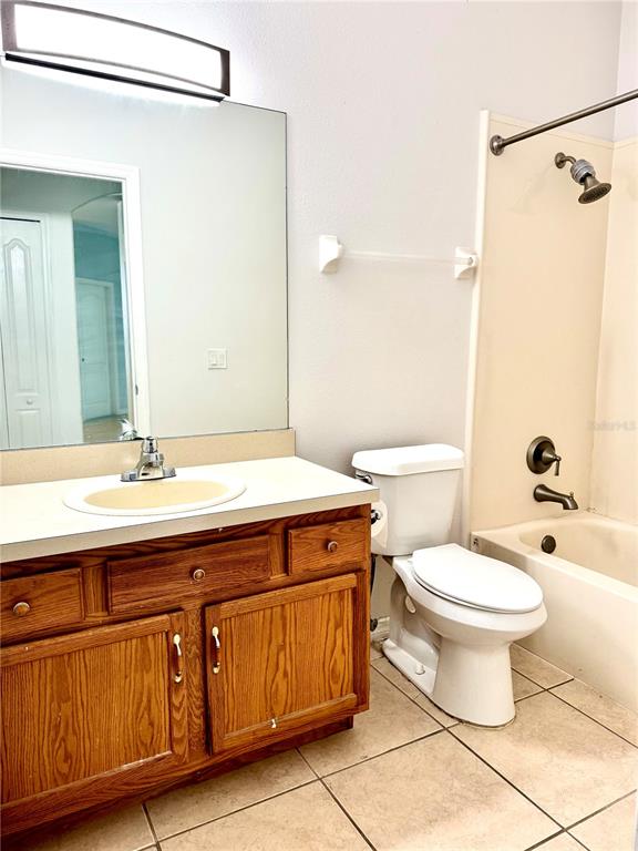A bathroom features a wooden vanity, a large mirror, a toilet, and a shower-tub combo — 1944 THE OAKS BOULEVARD, KISSIMMEE, FL