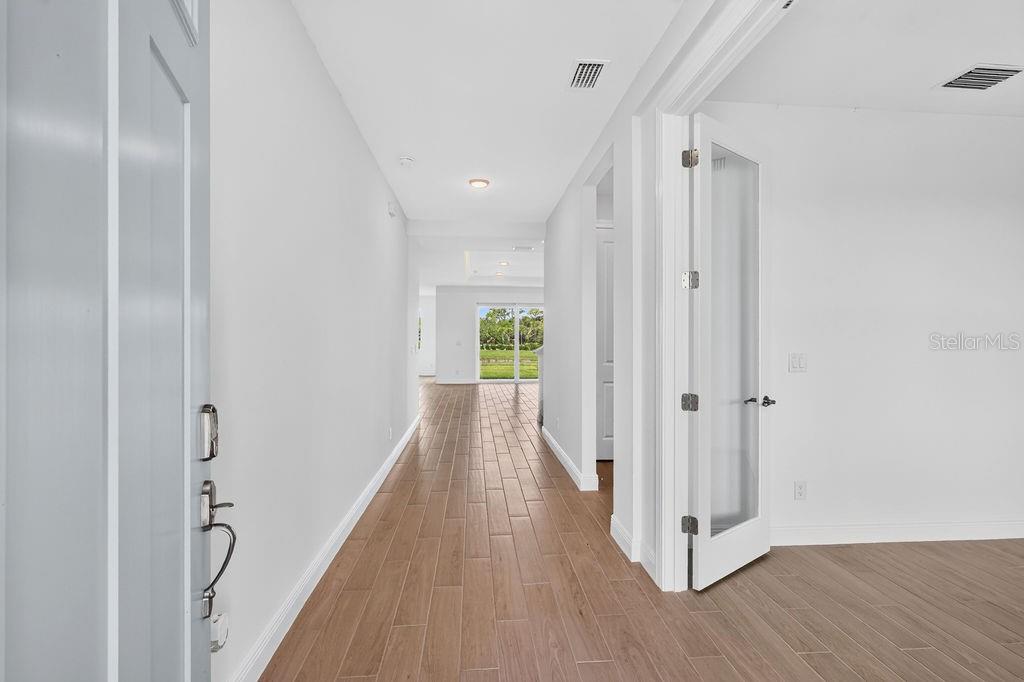 A hallway with wood-look tile flooring leads toward a glass door viewing a backyard — 15692 ROSEBUD COURT, PUNTA GORDA, FL