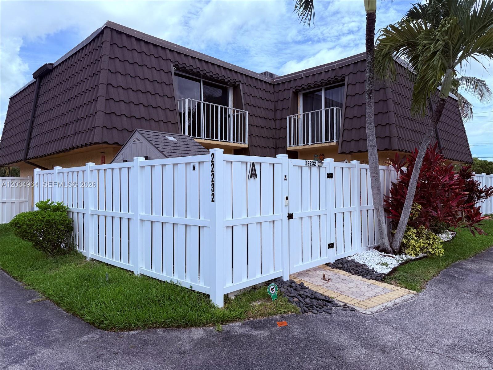 A white vinyl fence encloses the front patio of a two-story building with brown roofing — BOCA RATON, FL