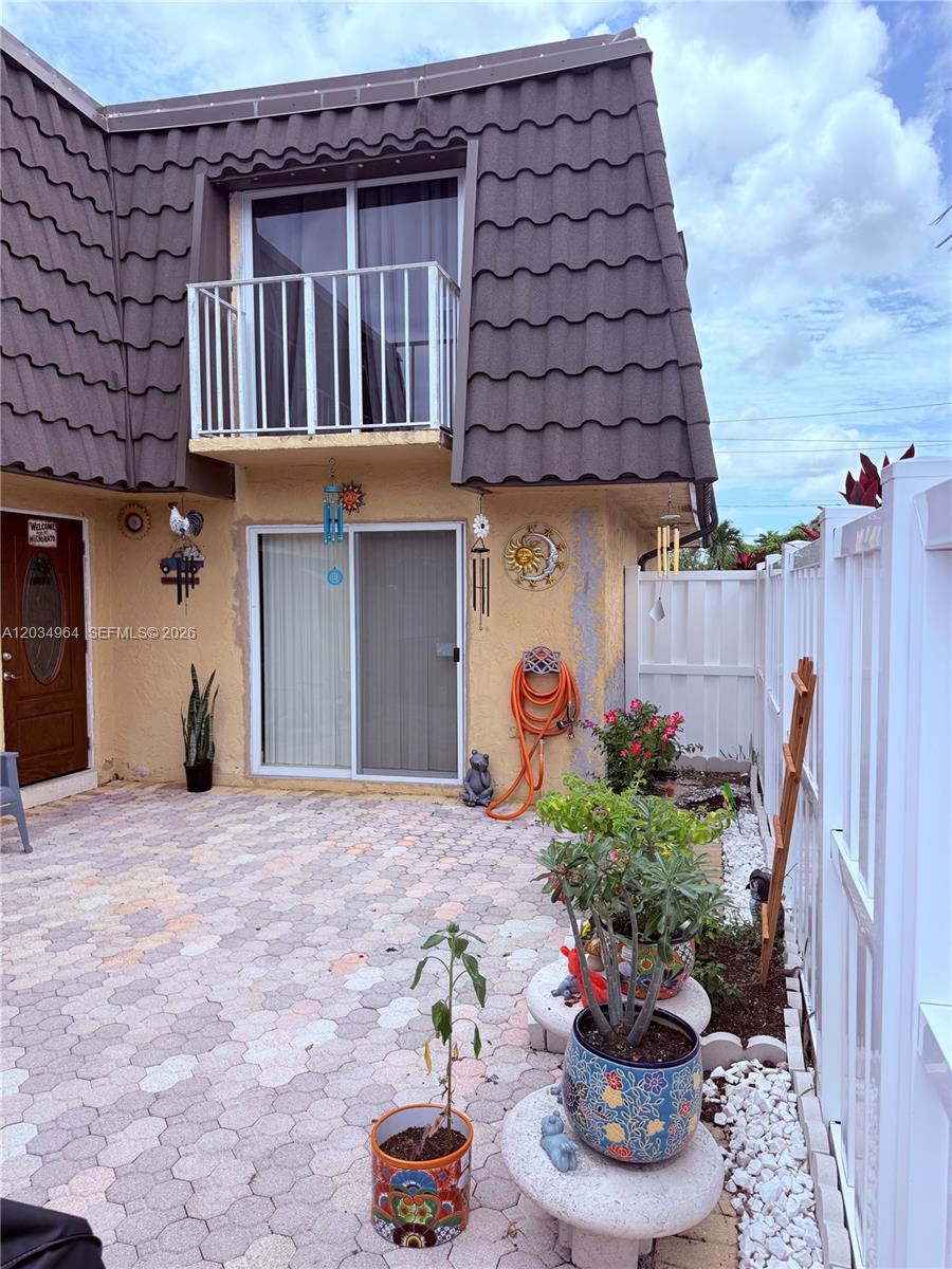 A patio with pavers, potted plants, and a sliding glass door leads to a balcony — BOCA RATON, FL