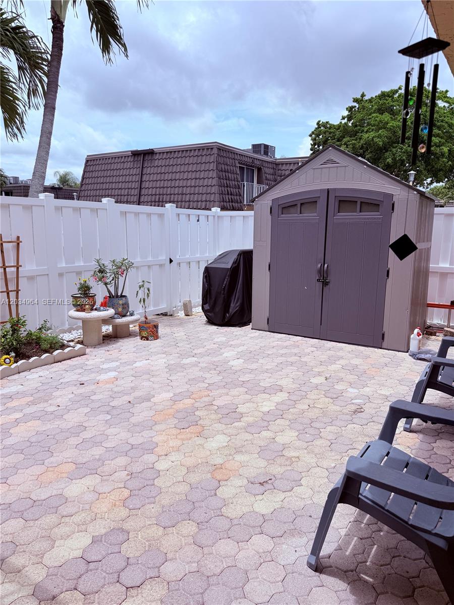 A paved patio features a storage shed, a covered grill, and potted plants against a fence — BOCA RATON, FL