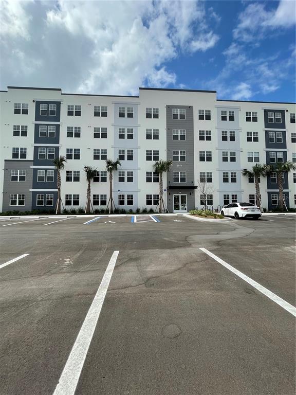 A multi-story apartment building with a large parking lot and palm trees in front — 5579 MILLENIA PARK UNIT 403, ORLANDO, FL