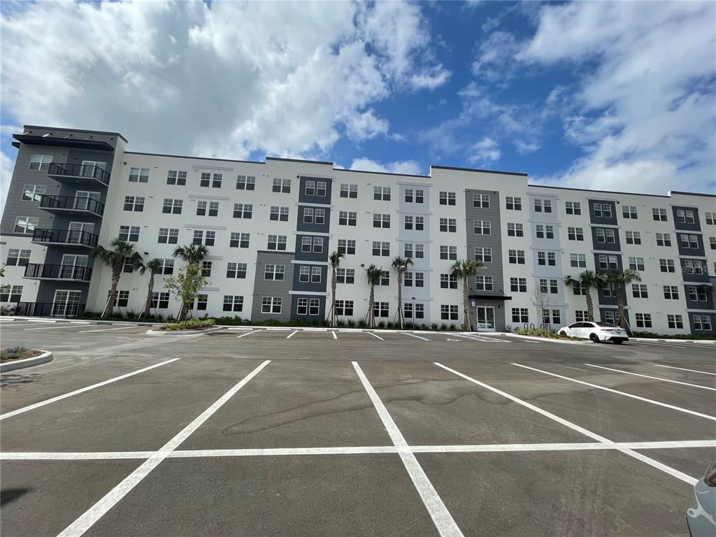 A multi-story apartment building features a large parking lot in the foreground — 5579 MILLENIA PARK UNIT 403, ORLANDO, FL