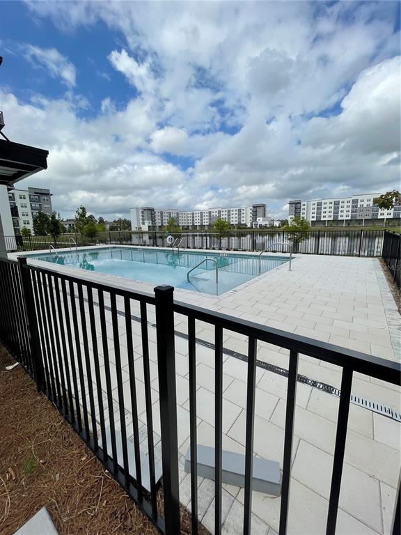 A swimming pool with a paved deck is enclosed by a black metal fence — 5579 MILLENIA PARK UNIT 403, ORLANDO, FL
