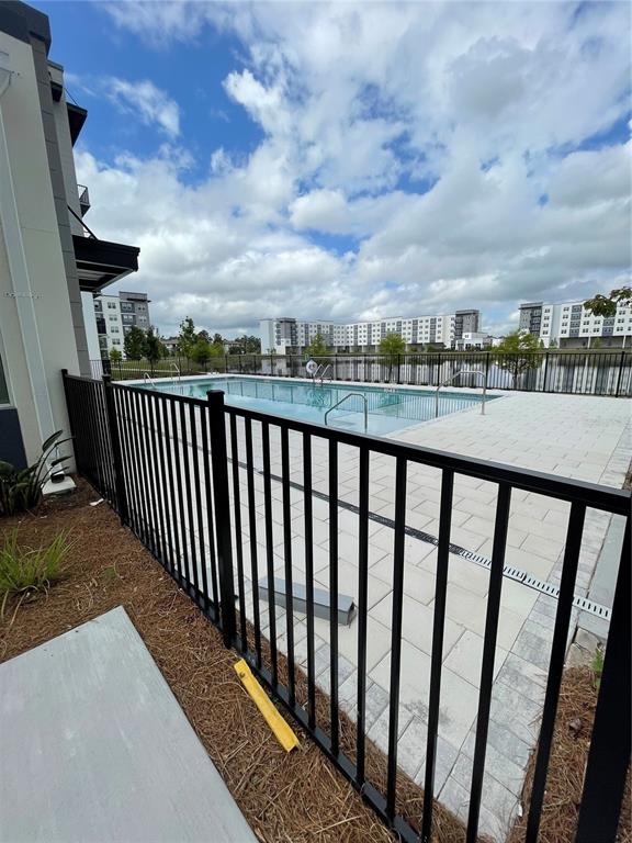 A black metal fence surrounds a swimming pool on a paved patio near apartment buildings — 5579 MILLENIA PARK UNIT 403, ORLANDO, FL
