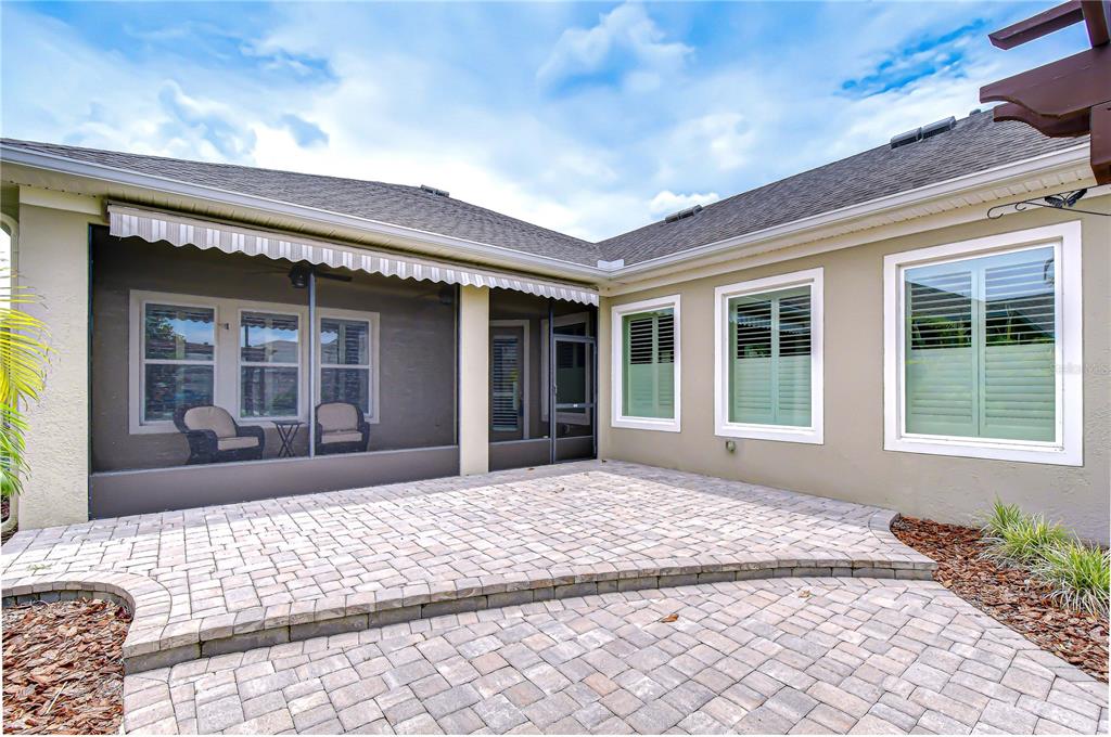 A paved patio sits outside a house with a screened-in porch and shuttered windows — 6005 SPARROWHEAD WAY, LITHIA, FL