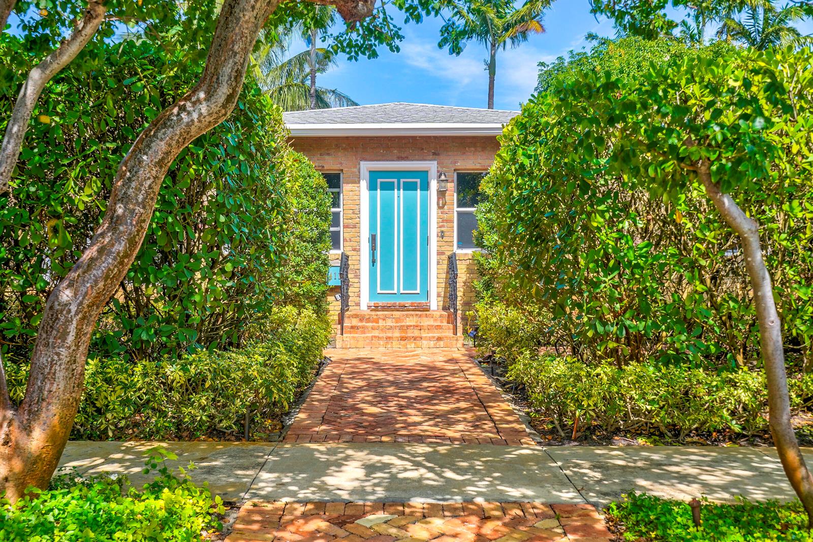 A brick walkway leads to a house entrance with a bright blue door and landscaping — 411 26th Street, West Palm Beach FL 33407, WEST PALM BEACH, FL