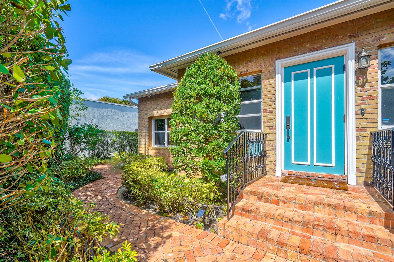 A brick house exterior features a bright blue front door, brick steps, and landscaped walkway — 411 26th Street, West Palm Beach FL 33407, WEST PALM BEACH, FL