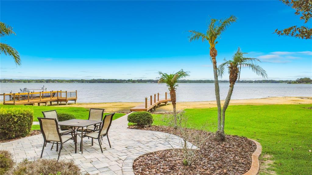 A patio with a dining set overlooks a sandy beach, a wooden dock, and a lake — 4703 CASSANDRA LANE, LAKELAND, FL