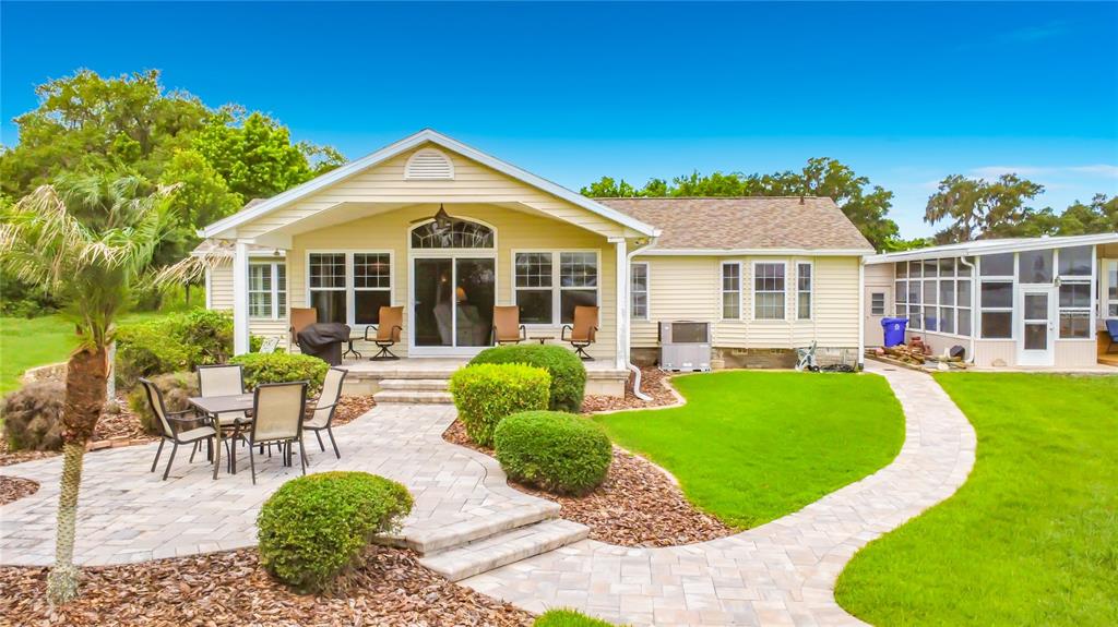 A yellow house features a paved patio, a manicured lawn, and a screened-in sunroom — 4703 CASSANDRA LANE, LAKELAND, FL